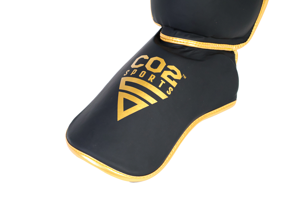 Black shin guard with gold accents and 'Cos Sports' logo on a white background